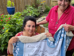 Mother and daughter sitting in a garden holding the Heirloom blanket with the mother's note to her daughter printed on it. The blanket is made of exceptionally soft faux mink with a sherpa back lining.